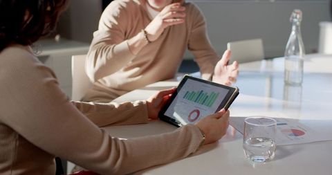 Diverse coworkers reviewing tablet analytics and charts during collaborative office meeting