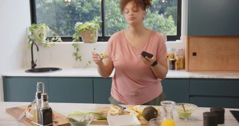 African American woman in 20s preparing healthy avocado breakfast at teal kitchen island