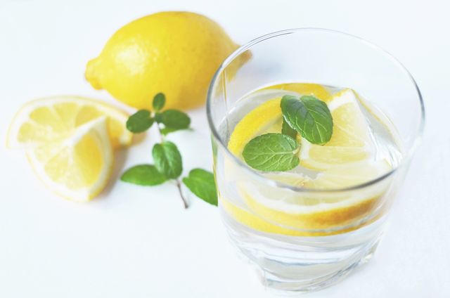 This image depicts a glass of water infused with lemon slices and mint leaves, set against a light background. Additionally, whole and sliced lemons with mint leaves are displayed beside the glass. This bright and fresh image can be used for creating content about healthy lifestyle choices, diet tips, detox drinks, or summer refreshers. It can also illustrate blog posts or articles related to wellness, healthy eating, and natural hydration solutions.