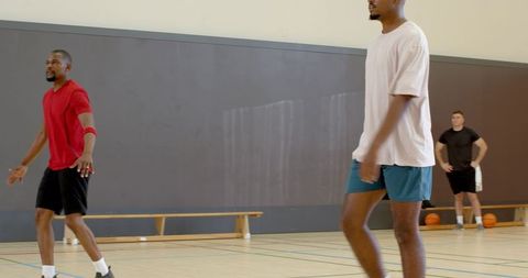 Male athletes walking on indoor basketball court practicing defense drills during training