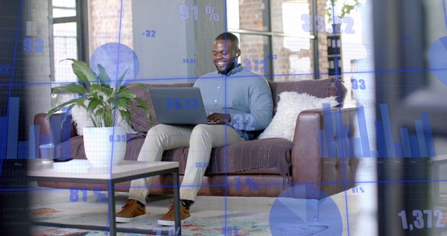 Man sitting on a couch at home using laptop to analyze stock market data, smiling while working remotely. Suitable for themes around remote work, tech-savvy business professionals, financial analytics, home office setups and the blend of home and professional environments.