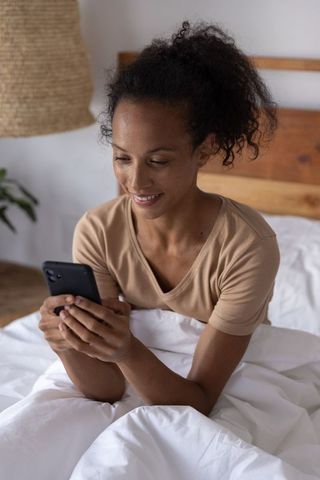 African american woman checking smartphone in cozy bedroom morning relaxed lifestyle scene