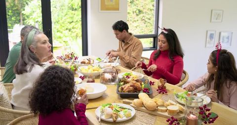 Multi-generation family sharing festive roast dinner at sunlit home dining table