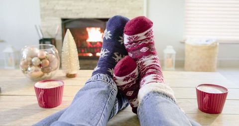 Couple relaxing by fireplace wearing festive patterned socks with hot cocoa on wood table