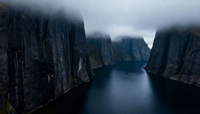 Mist-clinging fjord channel between steep granite cliffs, moody coastal gorge