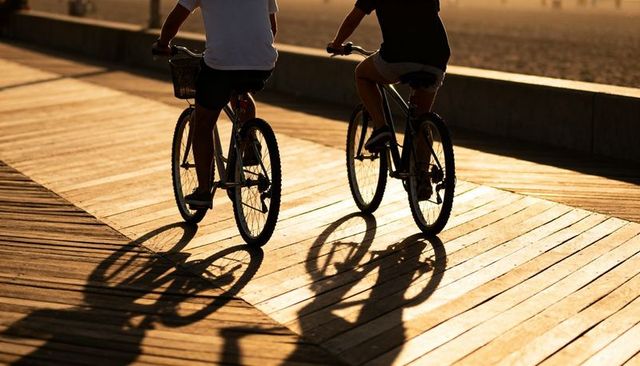 Couple riding bicycles on sunlit boardwalk at golden hour with long shadows