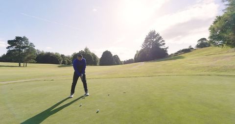 Golfer Performing Putt Shot on Green Lawn Under Bright Sunlight