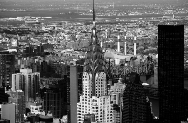 Black and white aerial view of the Chrysler Building in New York City with surrounding skyscrapers and urban landscape. Suitable for use in articles about travel, architecture, urban planning, and New York City landmarks. Perfect for history or architecture projects and as a striking wall art piece.