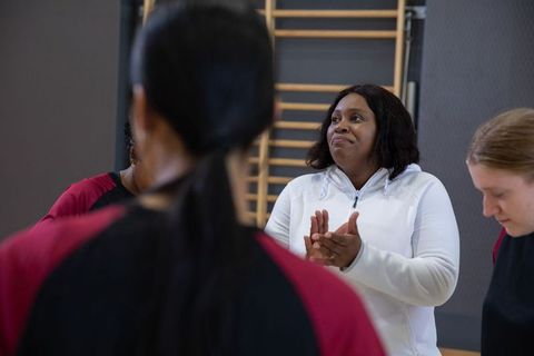 African american coach leading team, clapping and encouraging during indoor gym training