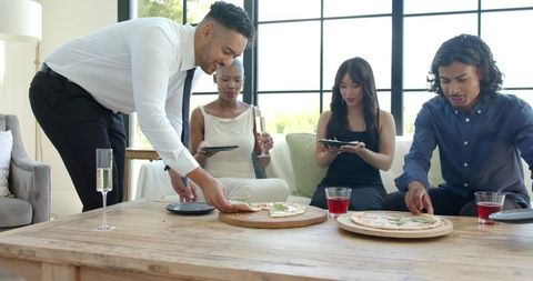 Multicultural friends sharing pizza and drinks in bright living room gathering