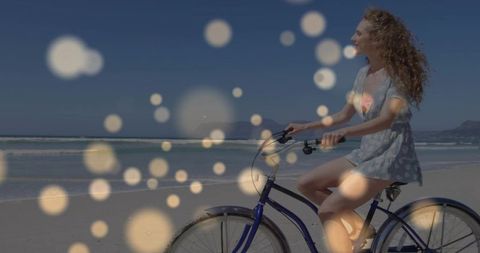 Young woman riding blue cruiser bicycle on sunny beach with dreamy bokeh and copy space
