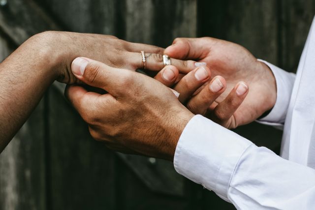 Close-up of two hands exchanging wedding rings signifies love and commitment. Perfect for use in wedding invitations, relationship building content, marital advice blogs, or anniversary celebration promotions.