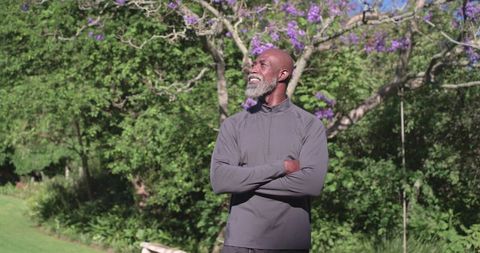 Senior african american man standing with arms crossed in sunlit garden with purple blooms
