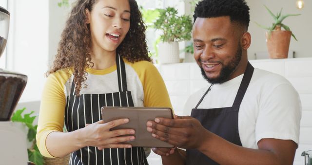 Happy african american male cafe owner and biracial female barista using tablet at cafe. small independent cafe business.
