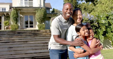 Happy Family of Four Embracing Outside Their Beautiful Home