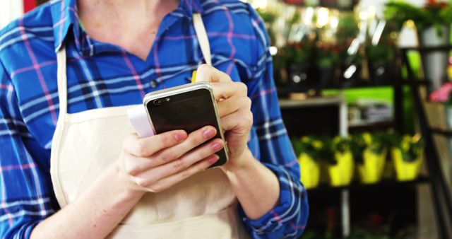 Female florist writing an order on notepad while using mobile phone in flower shop