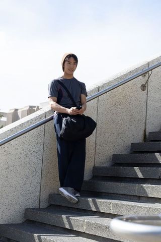 Asian man leaning on handrail holding phone and duffel on urban concrete stairs