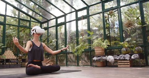 Woman Using VR Headset for Yoga and Meditation in Glasshouse