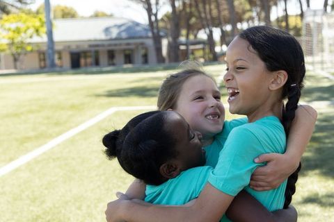 Girls celebrating team victory with group hug on youth soccer field wearing teal shirts