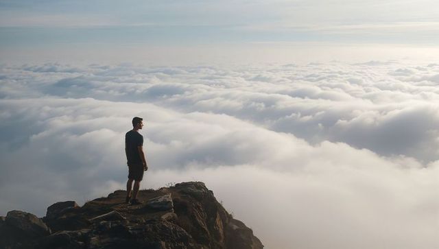 Hiker standing on cliff gazing over sea of clouds at mountain summit sunrise