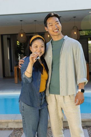Young asian couple celebrating new home by pool holding key fob