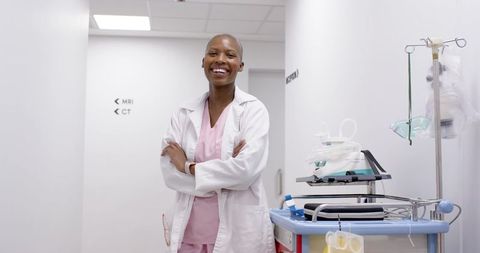 Smiling Medical Professional Standing in Hospital Corridor with Equipment Cart and IV Pole