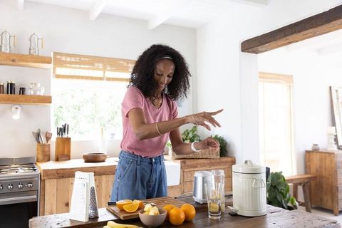 African american woman making fresh citrus juice on kitchen island, bright morning routine