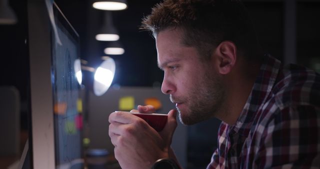 Man drinking coffee while working late at computer in dimly lit office - Download Free Stock Images Pikwizard.com