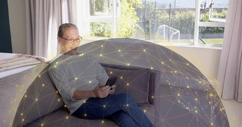 Senior chinese woman using smartphone on sofa with digital network overlay for smart home