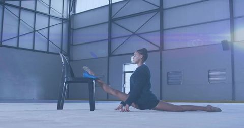 Athlete practicing split stretch on rink with chair for flexibility training
