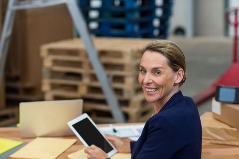 Businesswoman Managing Warehouse Operations with Tablet and Laptop