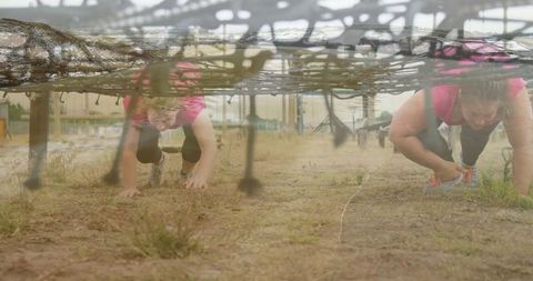 Women crawling under rope net in obstacle course