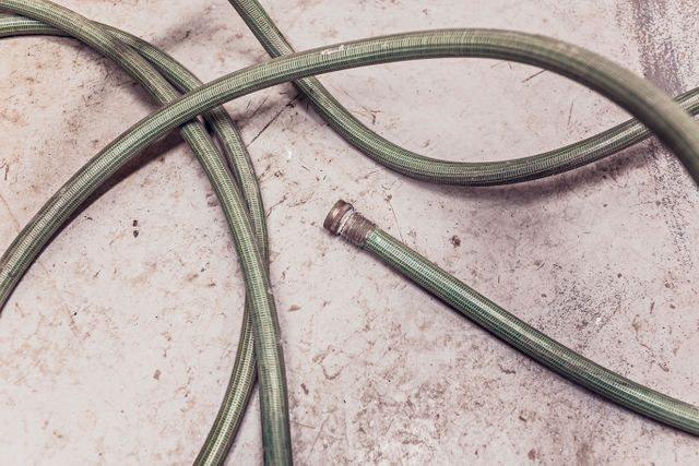Water hose laying on concrete floor showing signs of wear and tear, ideal for illustrating DIY projects, household maintenance, outdoor gardening equipment or issues with water pipes.