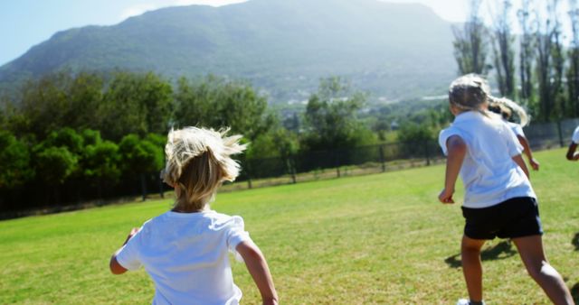 Capturing the joy of childhood, this photo shows children running on a grassy field with a beautiful mountain view in the background. Ideal for use in advertisements for outdoor activities, youth programs, summer camps, or sports events. The image conveys themes of energy, freedom, and connection with nature.