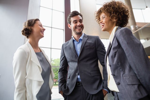 Business executives in professional attire are smiling and engaging in a lively discussion at a conference center. This image is ideal for illustrating concepts related to teamwork, collaboration, networking, and corporate environments. It can be used in business presentations, corporate websites, marketing materials, and articles about business communication and professional interactions.