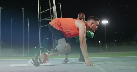 Prosthetic athlete preparing for race with coach guidance at night