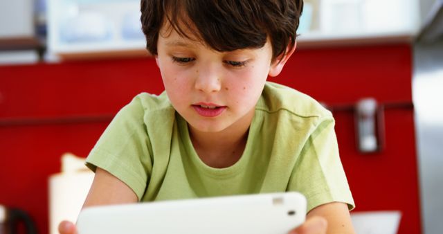 Young boy in green shirt using a tablet indoors, looking focused and curious. Can be used for topics related to education, childhood, technology, and learning at home.