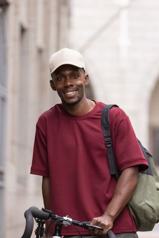Smiling urban cyclist with backpack standing beside bicycle in narrow stone archway