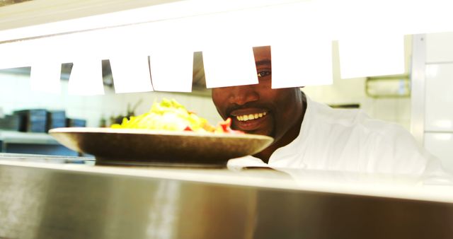 Chef in professional kitchen, smiling while presenting a freshly prepared dish. Perfect for illustrating restaurant services, professional culinary environments, or food service advertisements.