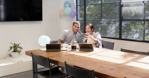 Joyful multiracial colleagues taking selfie with balloons at office celebration