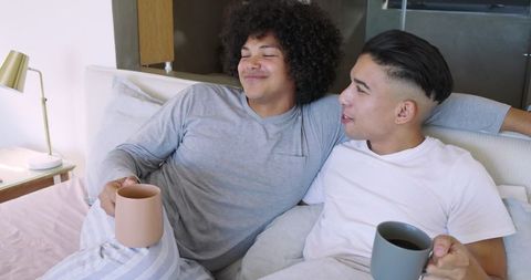 Diverse pair enjoying coffee in bed, relaxing with morning cup