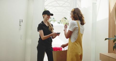 Courier delivering takeout to customer in bright minimalist entryway using mobile scanner