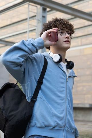 Teen male talking on phone wearing headphones and backpack at urban transit shelter