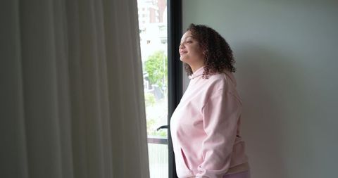 African american woman at balcony door wearing pink hoodie enjoying calm morning light