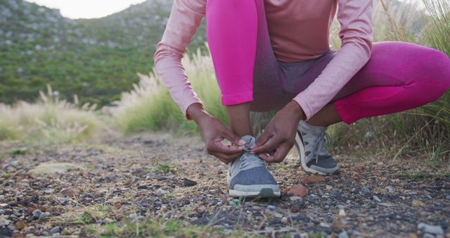 Woman preparing for a fitness routine by tying running shoes on a scenic outdoor trail. Suitable for illustrating concepts related to health, exercise, natural lifestyle, and outdoor activities. Perfect for fitness, sportswear advertisements, or health and wellness websites.