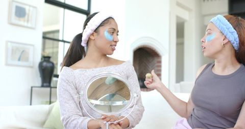 African american friends sharing at-home skincare routine with eye patches and mirror
