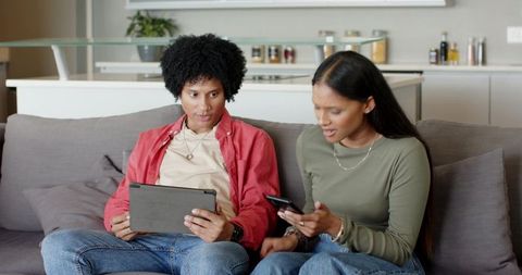 Two friends using tablet and smartphone in modern living room