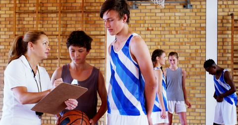 Basketball coach guiding team of young players in gym