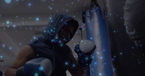 Hooded boxer training with heavy bag and blue particle light effect for intense gym mood