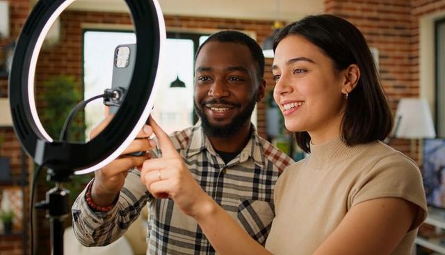 Smiling Creator Duo Adjusting Smartphone on Ring Light in Bright Loft Workspace